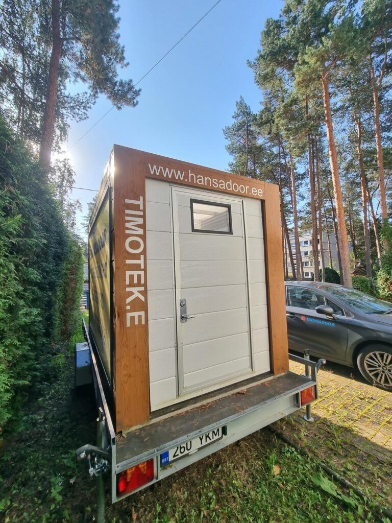 Metsases alal pargitud autode lähedal haagisel seisab väike valge uksega moodulhoone, millel on sildid "TIMOTEKE" ja "www.hansadoor.ee" – ideaalne neile, kes otsivad leiunurki, näiteks kasutatud garaažiuksi.